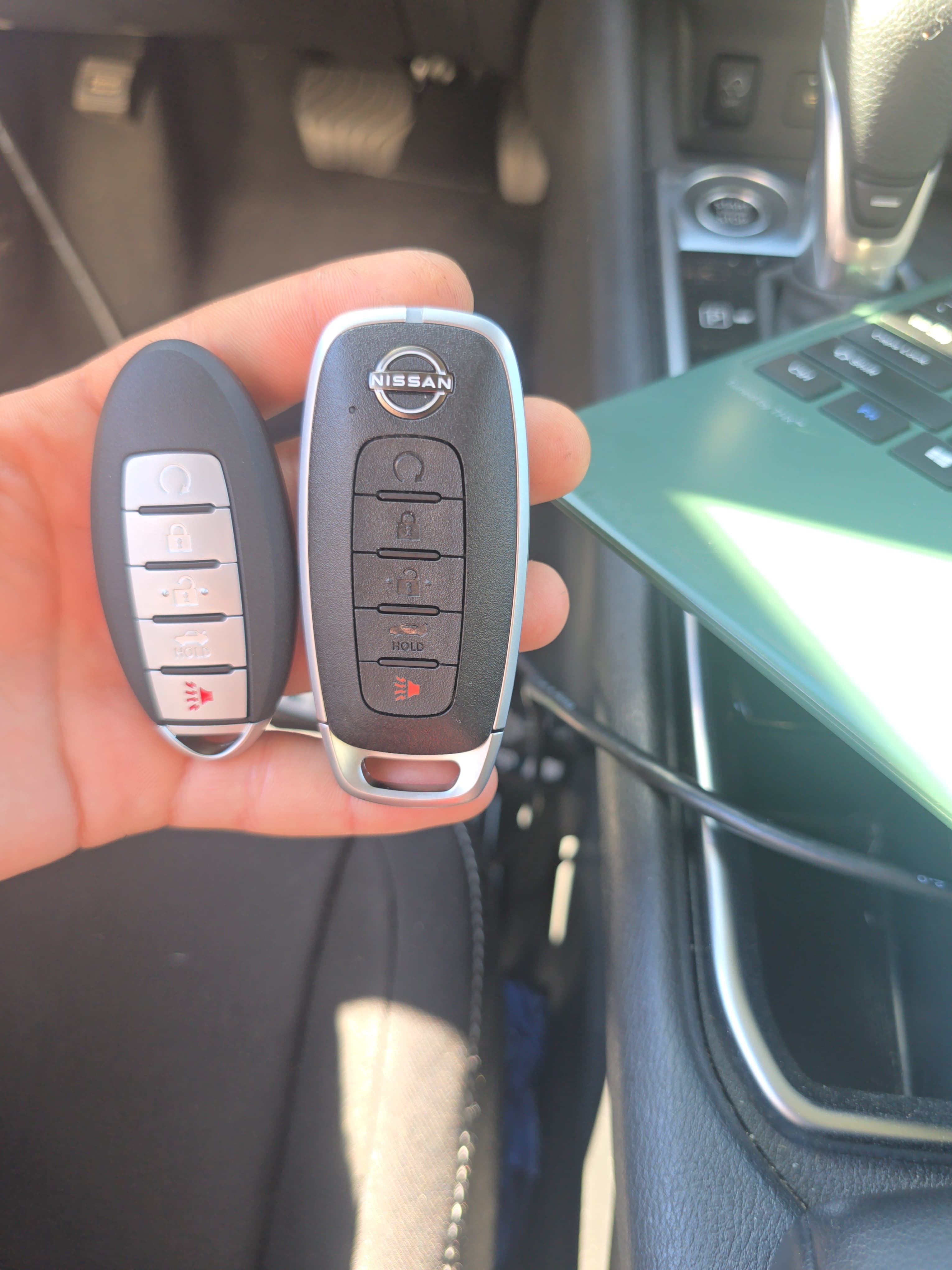 Hand holding a black and a silver Nissan key fob inside a car's cabin.