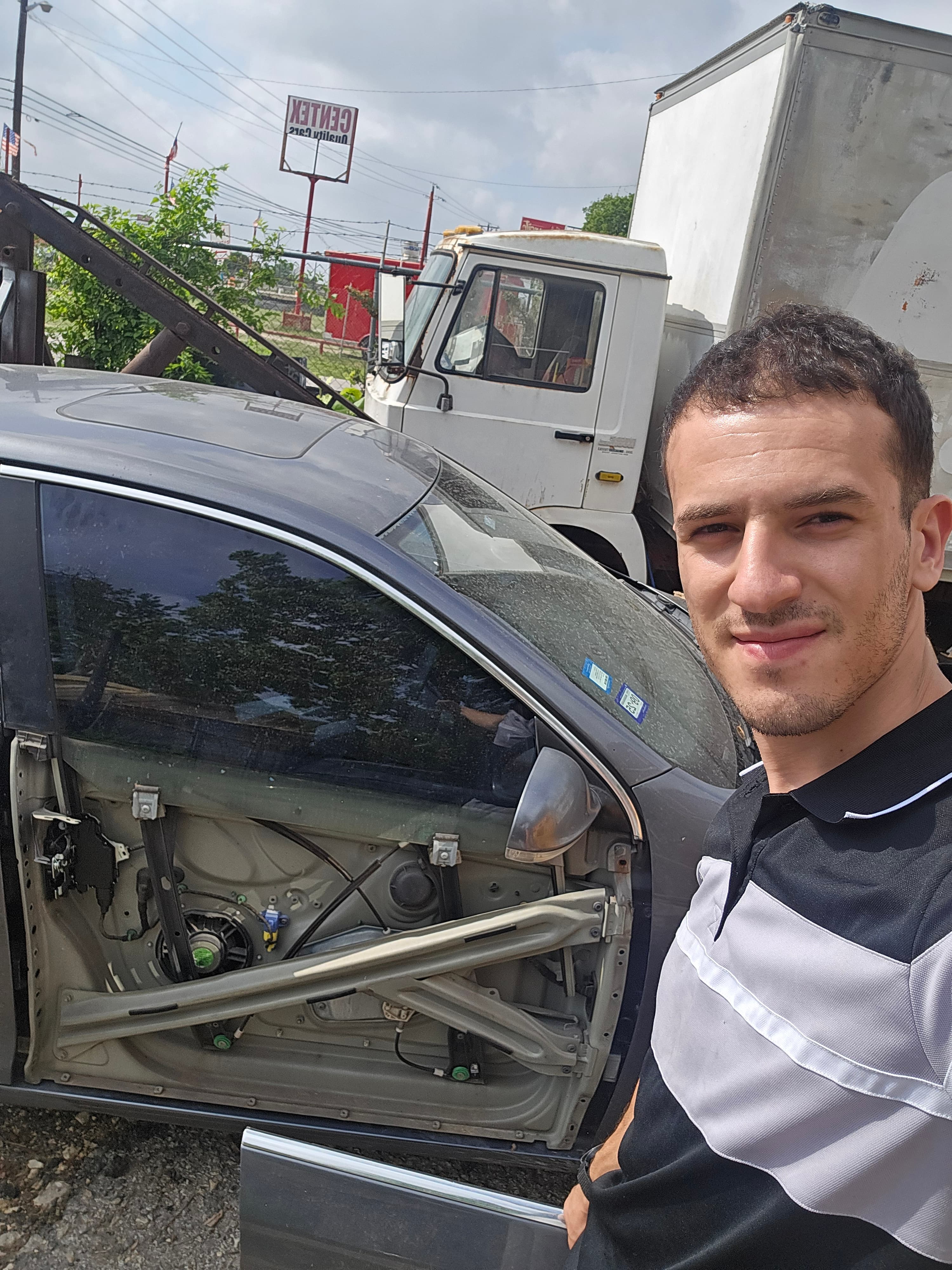 Man posing for a selfie beside a car with its interior door panel removed.