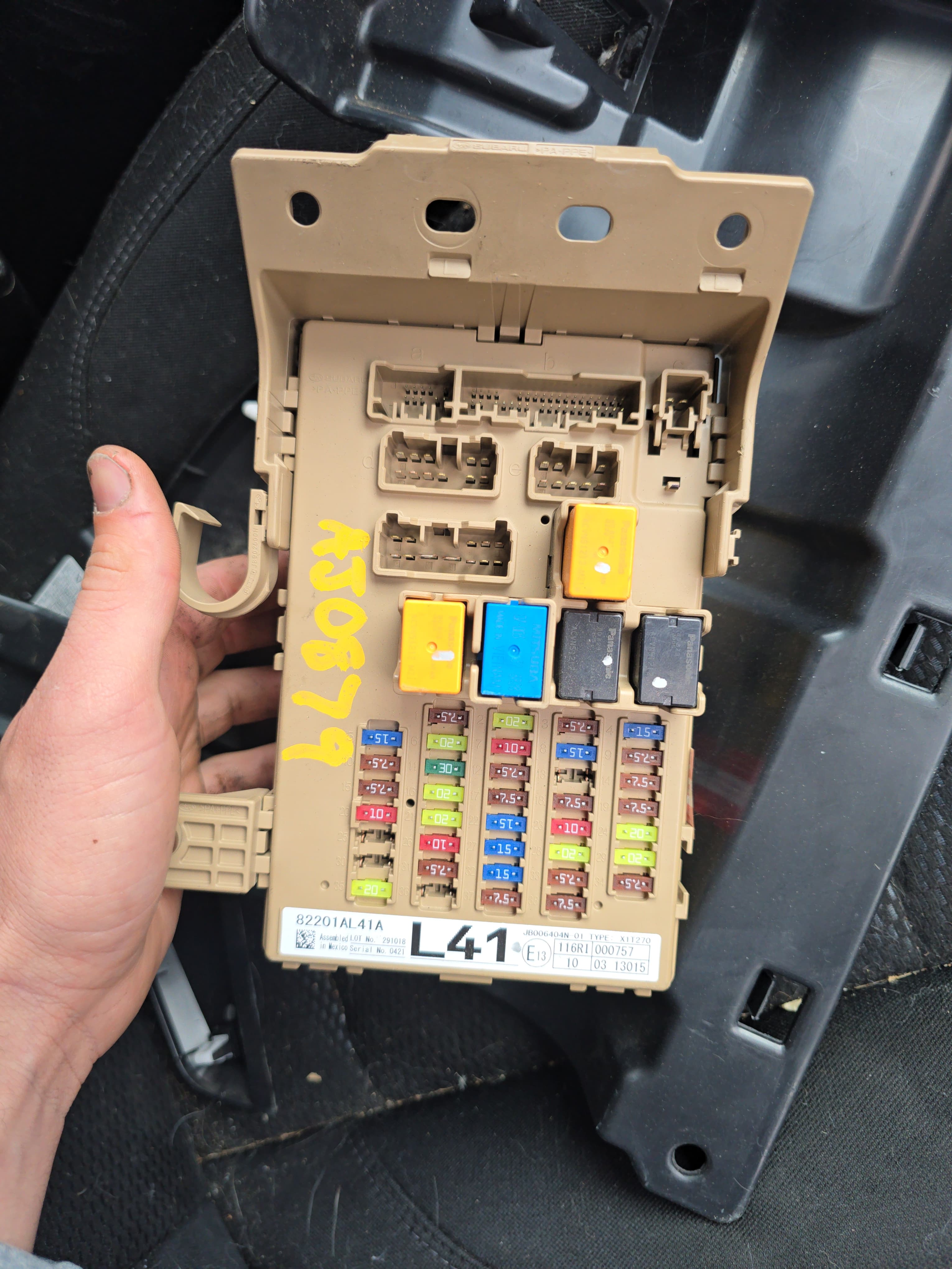 Tan car fuse box with colorful fuses, relays, and yellow markings, held by a hand.