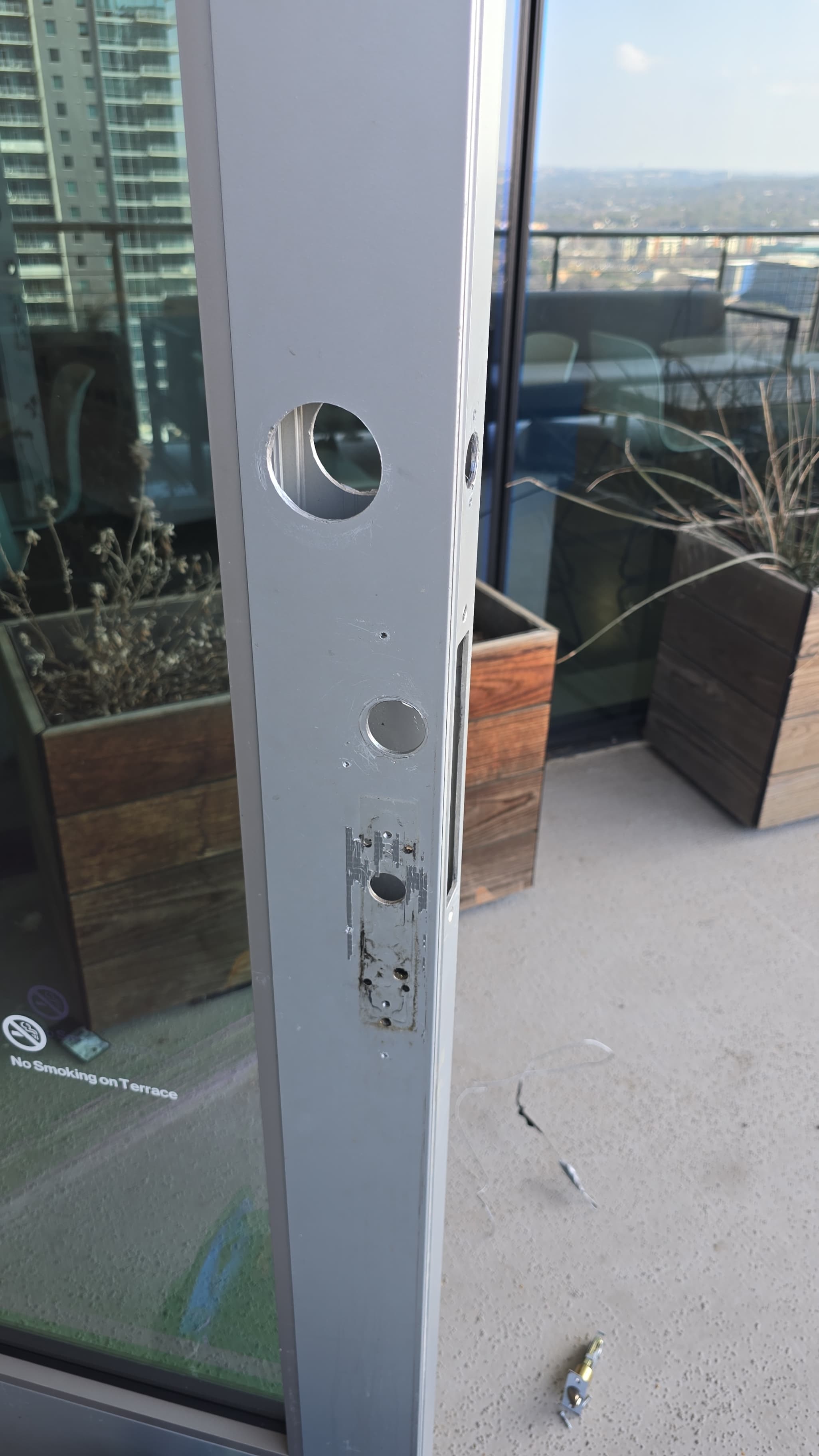 Silver metal door frame with empty holes and scratches from a removed lock mechanism.